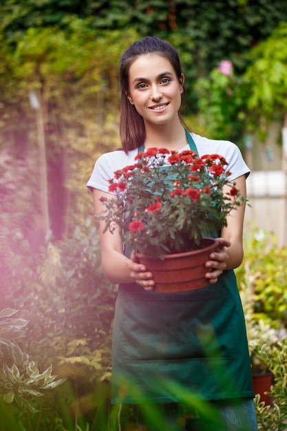 Floristería hermosa joven posando, sonriendo entre flores.