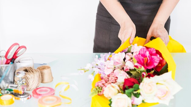 Floristería a mano envolviendo flores en tela amarilla.