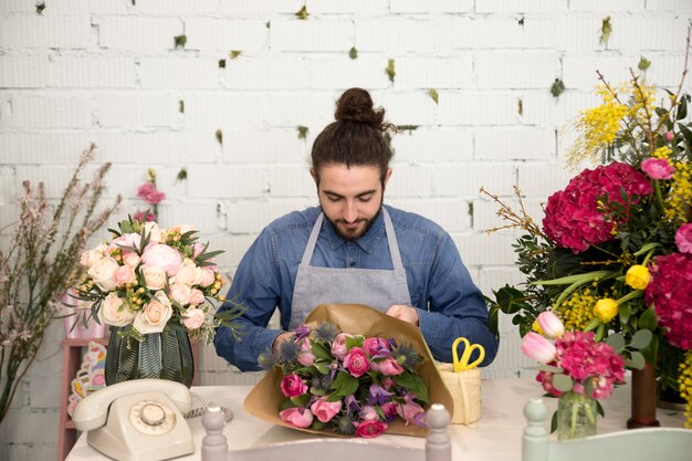 Floristería masculina envolviendo el ramo de flores en el papel en su floristería