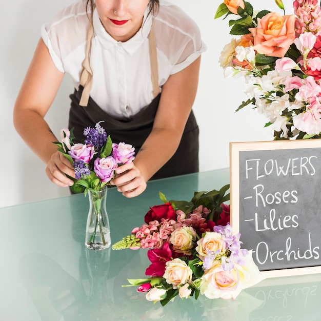 Floristería mujer arreglando flores en el florero en el escritorio de vidrio