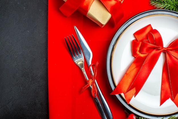 Fondo de año nuevo con cinta roja en el plato de cena cubiertos accesorios de decoración ramas de abeto junto a un regalo en una servilleta roja