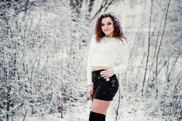 Fondo de chica morena rizada que cae ropa de nieve en minifalda negra y medias de lana Modelo en invierno Retrato de moda en clima nevado Instagram foto tonificada