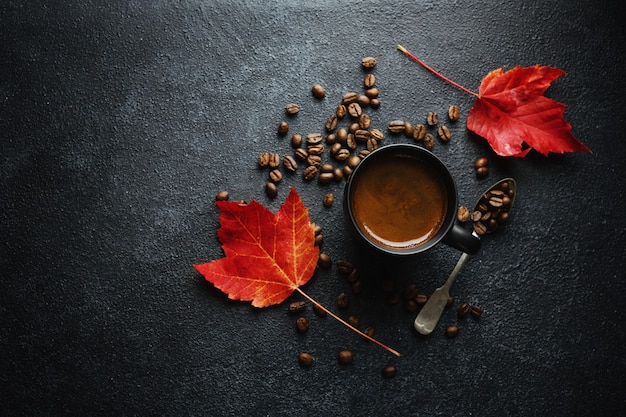 Fondo de concepto de otoño con hojas de otoño y café servido en taza sobre fondo oscuro.