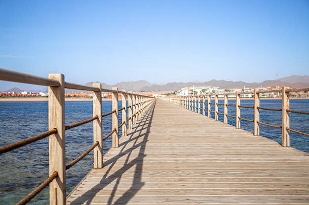 El fondo es un hermoso muelle de madera largo entre el océano y las montañas.