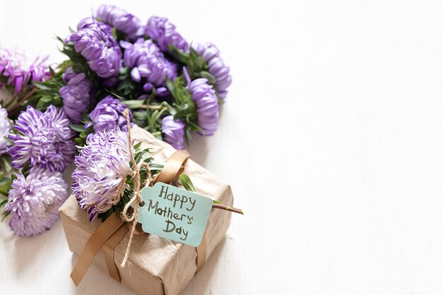 Fondo festivo del día de las madres con caja de regalo y flores de crisantemo frescas sobre fondo blanco, espacio de copia.