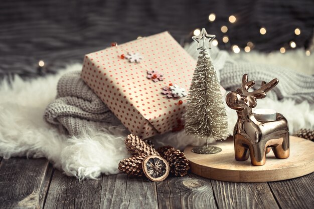 Fondo festivo de Navidad con ciervos de juguete con una caja de regalo, fondo borroso con luces doradas, fondo festivo en la mesa de la terraza de madera y suéter acogedor en el fondo