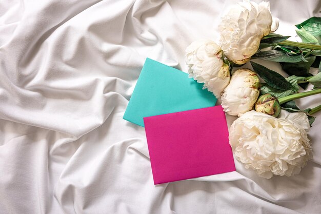 Fondo con flores peonías y sobres en la cama.