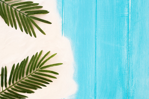 Fondo de madera azul claro con arena y hoja de palma, fondo de verano