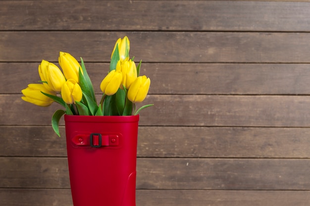 Fondo de madera con bota de agua y tulipanes amarillos