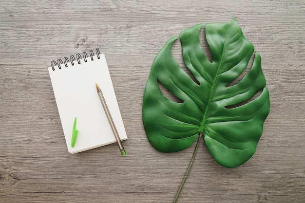 Fondo de madera con cuaderno en blanco y hoja de palma