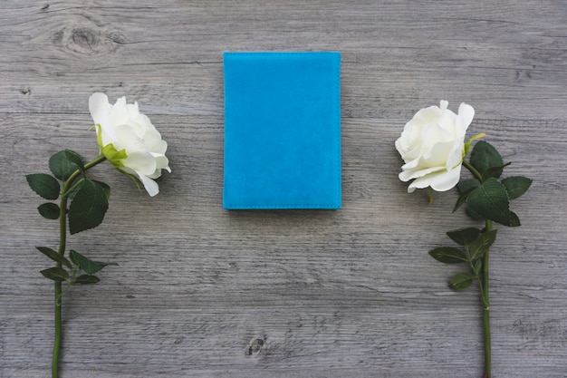 Fondo de madera con libro azul y dos flores blancas