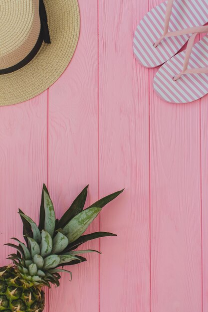 Fondo de madera rosa con chanclas, sombrero y piña