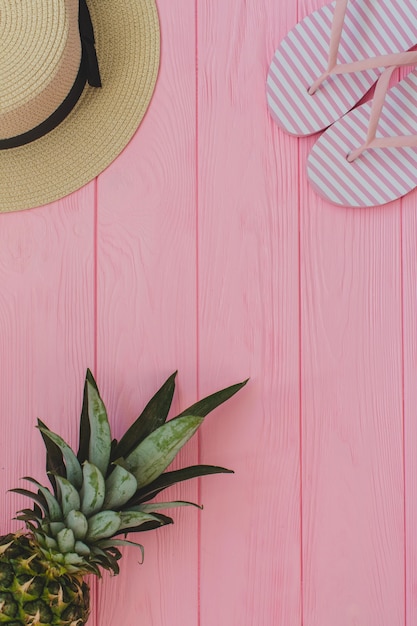 Fondo de madera rosa con chanclas, sombrero y piña