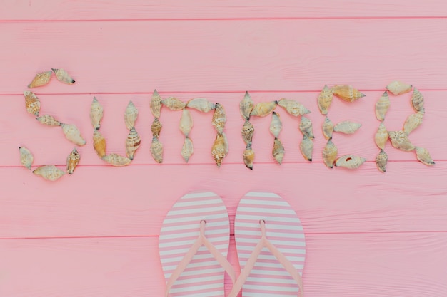 Fondo de madera rosa con conchas marinas y chanclas