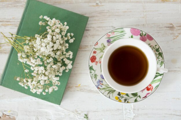 Fondo de madera con taza de café, flores y libro