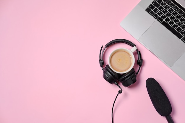 Fondo de música o podcast con auriculares, micrófono, café y computadora portátil en la mesa rosa plana Vista superior plana