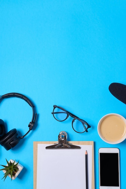 Fondo de música o podcast con auriculares, micrófono, café y espacio en blanco en la mesa azul plana Vista superior plana