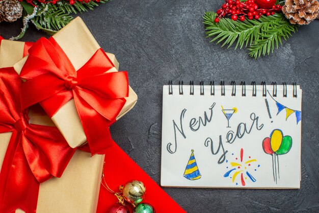 Fondo de navidad con hermosos regalos con cinta en forma de arco y accesorios de decoración de ramas de abeto cuaderno sobre una mesa oscura