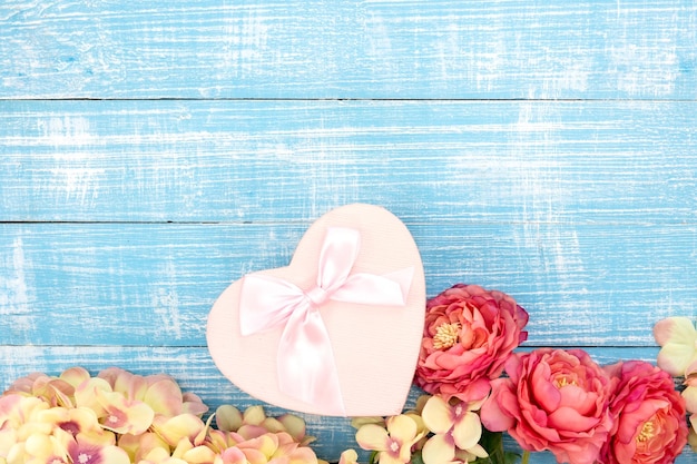 Foto gratuita fondo de primavera con flores y una caja de regalo en forma de corazón sobre un fondo azul.