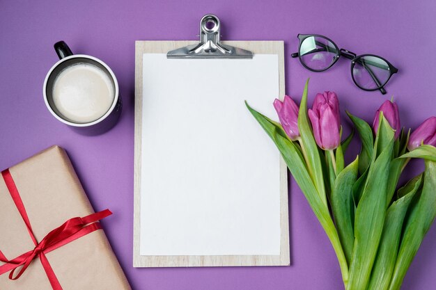 Fondo de tiempo de primavera con tulipanes morados en blanco vacíos blancos y una taza de café sobre un fondo violeta Vista superior plana