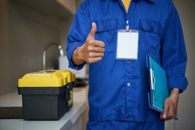 Foto gratuita fontanero masculino irreconocible de pie cerca del fregadero de la cocina y mostrando el pulgar hacia arriba