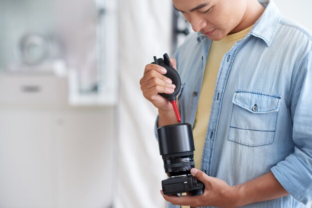 Foógrafo masculino asiático que limpia la lente de la cámara con el ventilador
