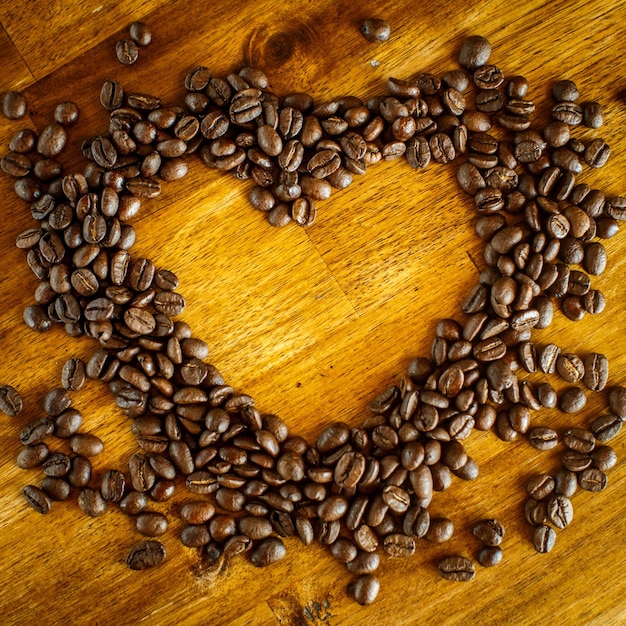 Forma de corazón hecha de granos de café sobre superficie de madera