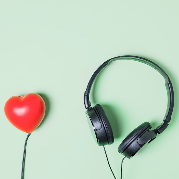 Forma de corazón rojo conectado a auriculares en fondo turquesa