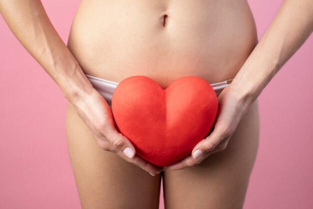 Forma de corazón sostenida por una mujer cerca de su sistema reproductivo