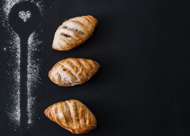 Forma de cuchara hecha con harina cerca de croissants sobre fondo negro