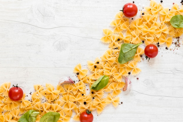 Foto gratuita forma curva elaborada con pasta farfalle y tomate. diente de ajo; hoja de albahaca sobre fondo de madera