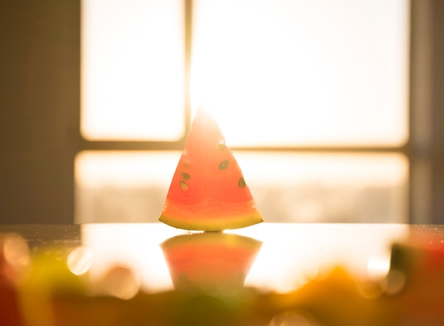 Forma triangular de sandía con semillas en una mesa reflectante bajo la luz del sol