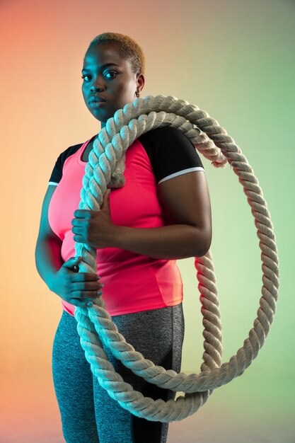 Formación de joven afroamericana de talla grande modelo femenina en pared degradada en luz de neón.