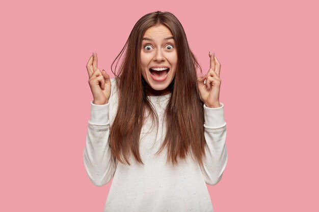 Foto de adolescente alegre y emotivo que mantiene los dedos índices cruzados, cree en algo maravilloso, mira con ojos saltones