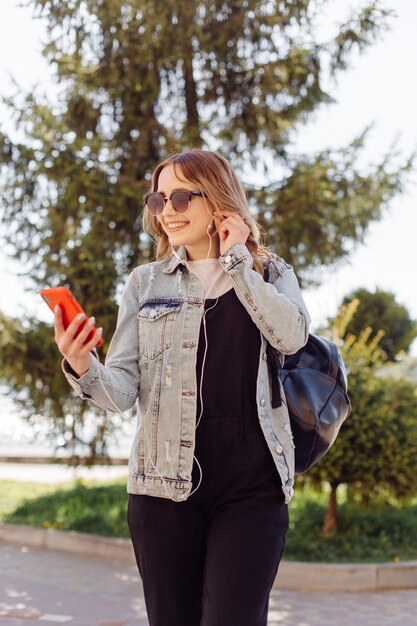 Foto de una adolescente alegre positiva pasa tiempo en el parque y usando el teléfono móvil.