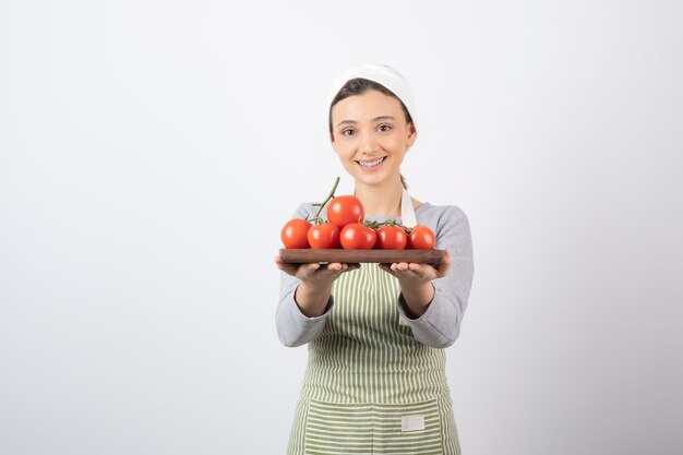 Foto de adorable joven sosteniendo un plato de tomates rojos sobre pared blanca