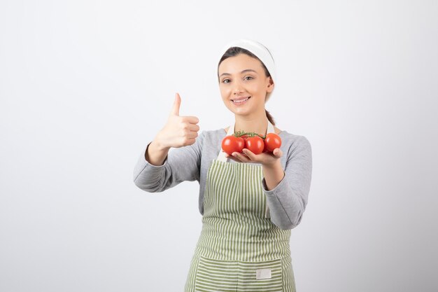 Foto de adorable joven sosteniendo tomates rojos y dando pulgar hacia arriba