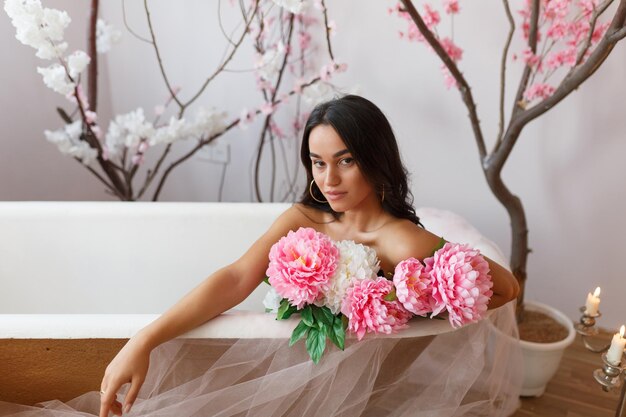 Foto de una adorable niña sosteniendo un ramo de flores de colores y sentada en una bañera Foto de alta calidad