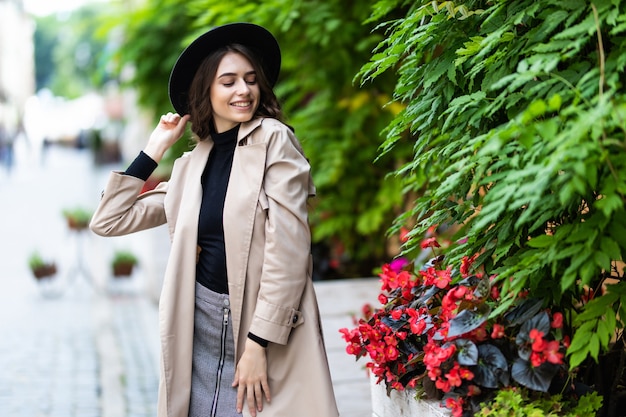 Foto al aire libre de moda de mujer joven bonita en traje elegante y sombrero negro caminando en la calle