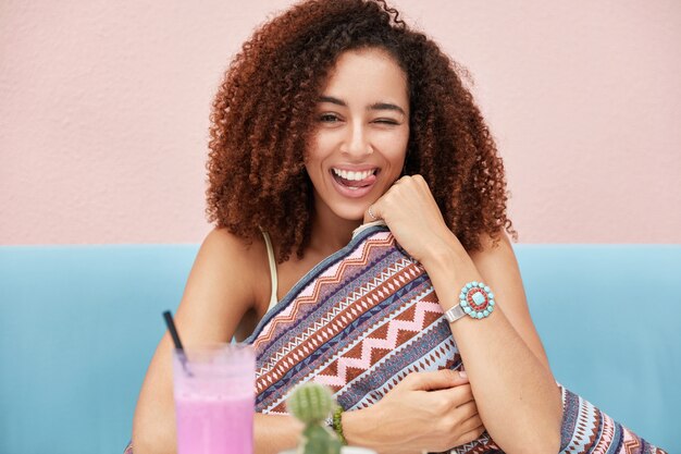 Foto gratuita foto de alegre divertida mujer afroamericana de piel oscura tiene el pelo muy rizado, parpadea y muestra la lengua