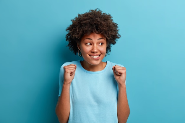 Foto de alegre mujer afroamericana aprieta los puños y espera algo agradable