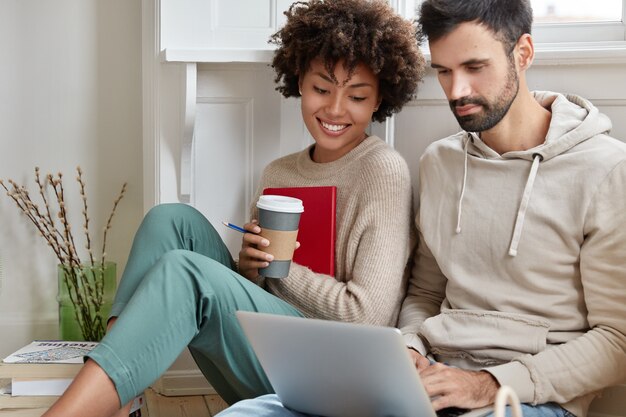 Foto de amigos varones y mujeres multirraciales felices ver videos en la computadora portátil, tener tiempo libre en casa.