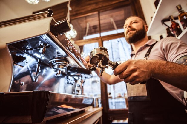 Foto de ángulo bajo de un barista sosteniendo un portafiltro, trabajando en la cafetería o restaurante