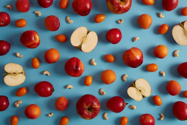 Foto anterior de manzanas rojas maduras, melocotones, tomarillo, cumquat y anacardos nutritivos sobre fondo azul. Composición creativa de deliciosas frutas. Alimentos dulces con viamins, concepto de nutrición saludable