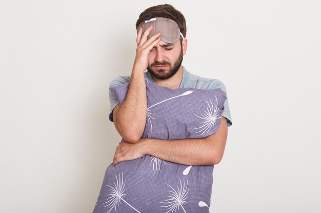 Foto de apuesto hombre caucásico posando aislado sobre blanco, experimentando dolor, se ve miserable y agotado