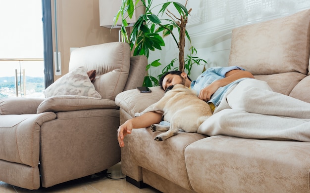 Foto de un apuesto hombre hispano durmiendo en un sofá con su perro