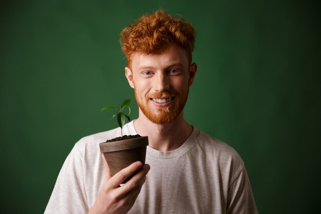 Foto de un apuesto joven pelirrojo con barba, sosteniendo una planta en maceta