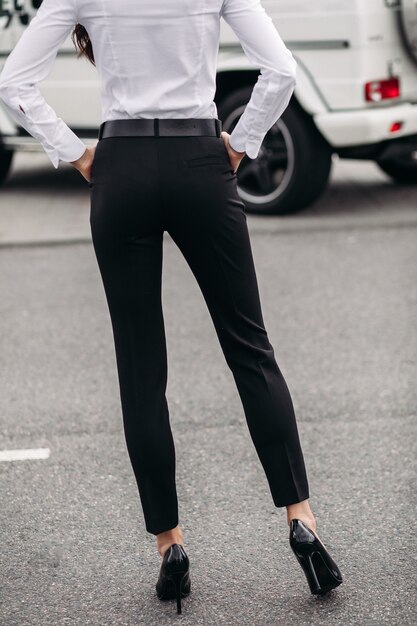 Foto de archivo recortada de una mujer irreconocible con camisa blanca y pantalón recto negro formal y tacones de cuero negro de pie en la calle. Modelo. Concepto de código de vestimenta.