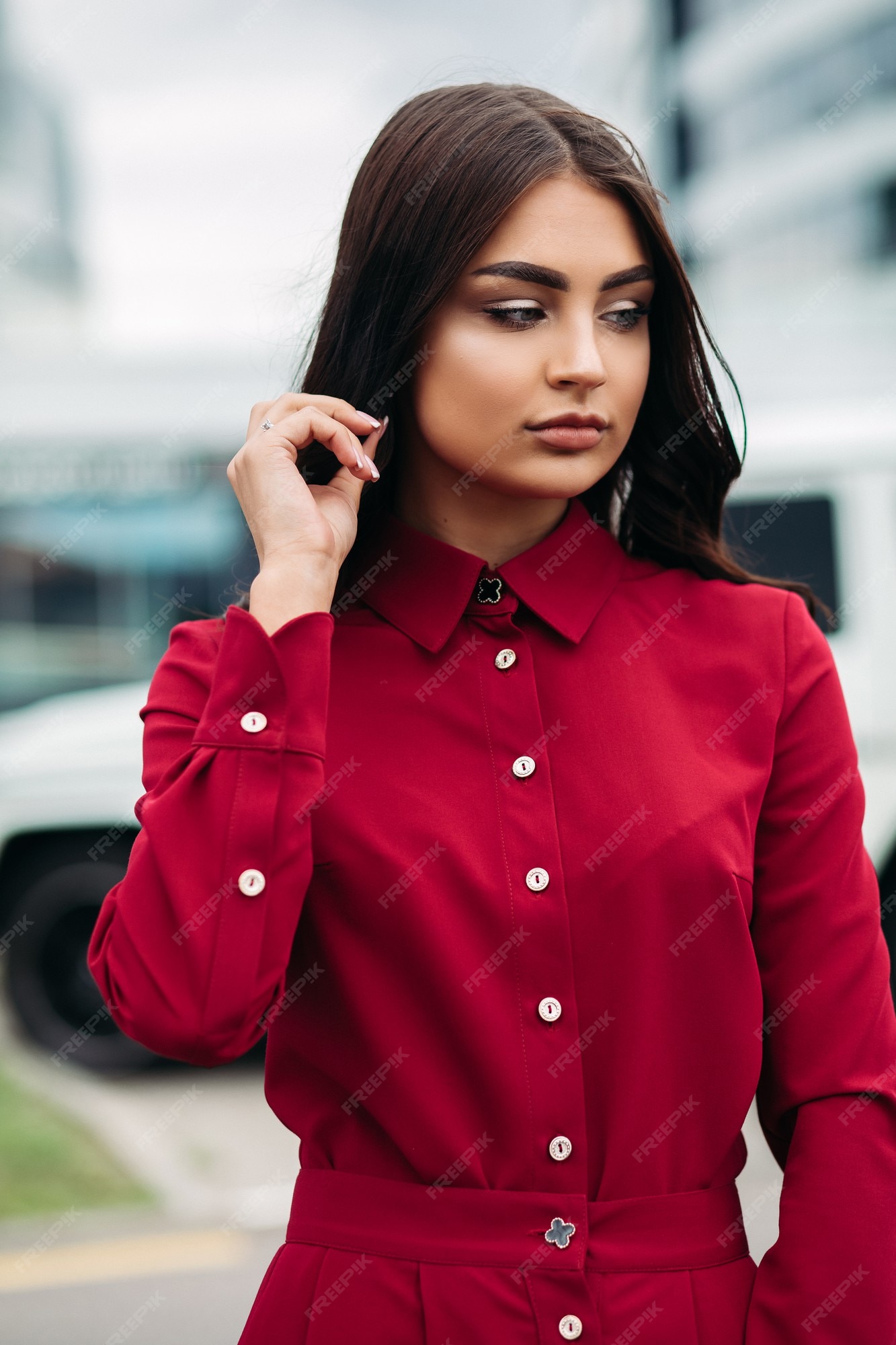 de archivo un modelo de moda con largo castaño y maquillaje con vestido rojo brillante con botones y cuello. tomando la mano en su cabello, mirando hacia otro