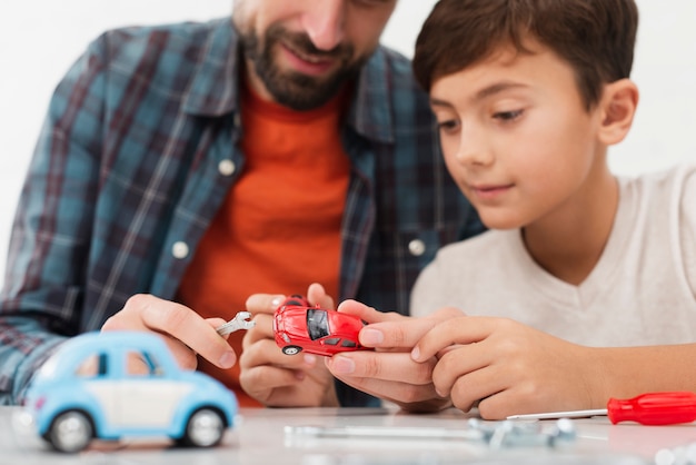 Foto artística hijo arreglando coches de juguete con padre